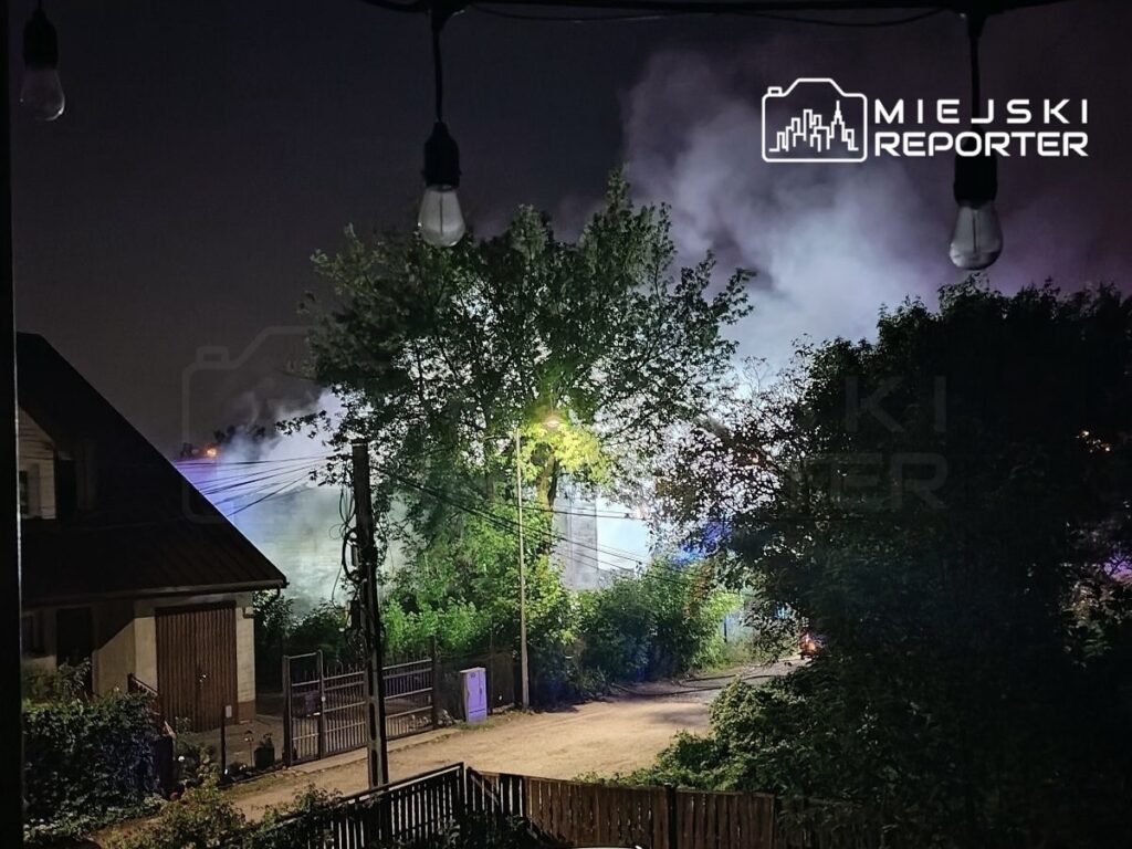 Gęsty dym unosi się nad osiedlem nocą, w tle widać oświetlenie służb ratunkowych.