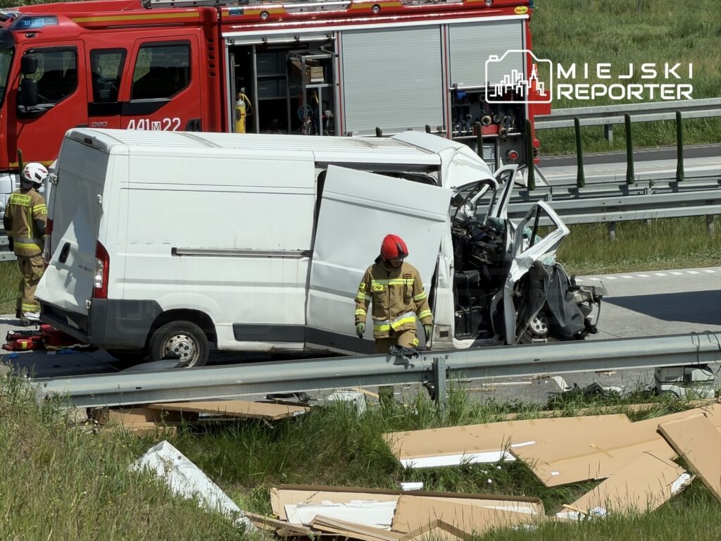 Wyspecjalizowany zespół straży pożarnej bada wypadek samochodowy na autostradzie, obok rozbitego furgonu.