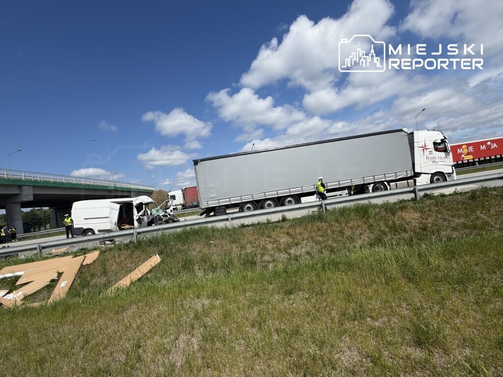 Wypadek drogowy z udziałem dostawczego samochodu osobowego i ciężarówki na autostradzie, obok policyjnych funkcjonariuszy.