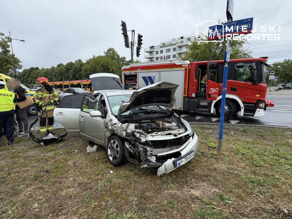 W miejscu wypadku drogowego, strażak w hełmie ocenia uszkodzenia rozbitego samochodu osobowego.