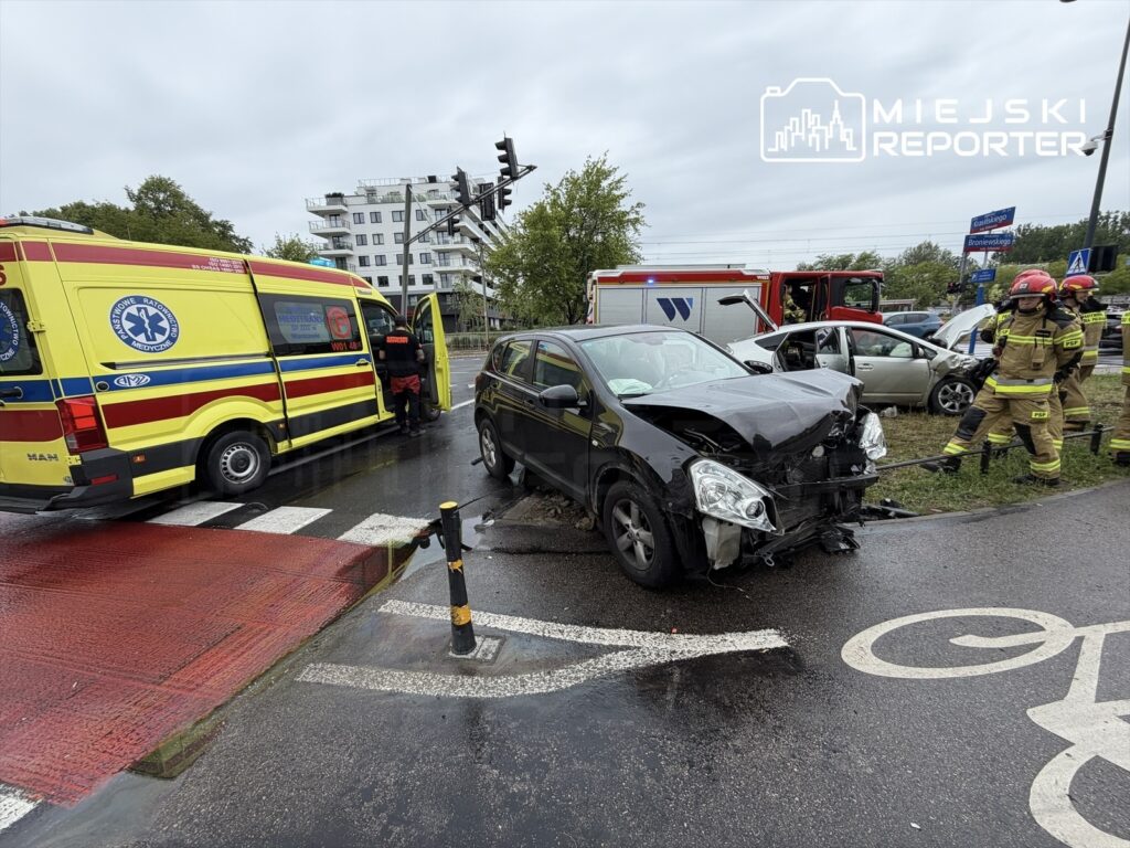 Zespół ratownictwa medycznego obsługuje wypadek drogowy, obok uszkodzonego samochodu w deszczowej scenerii.