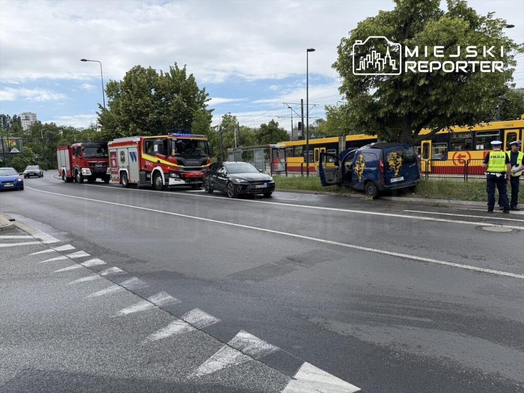 Samochód dostawczy stoi na poboczu drogi, obok interweniujący strażacy i policjanci, w tle tramwaj.
