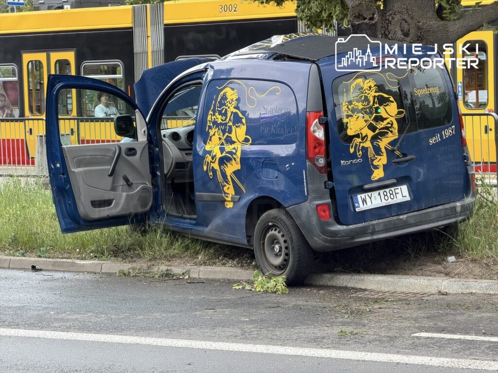 Niebieski samochód dostawczy z otwartymi drzwiami zaparkowany obok trawnika, w tle przejeżdżający tramwaj.