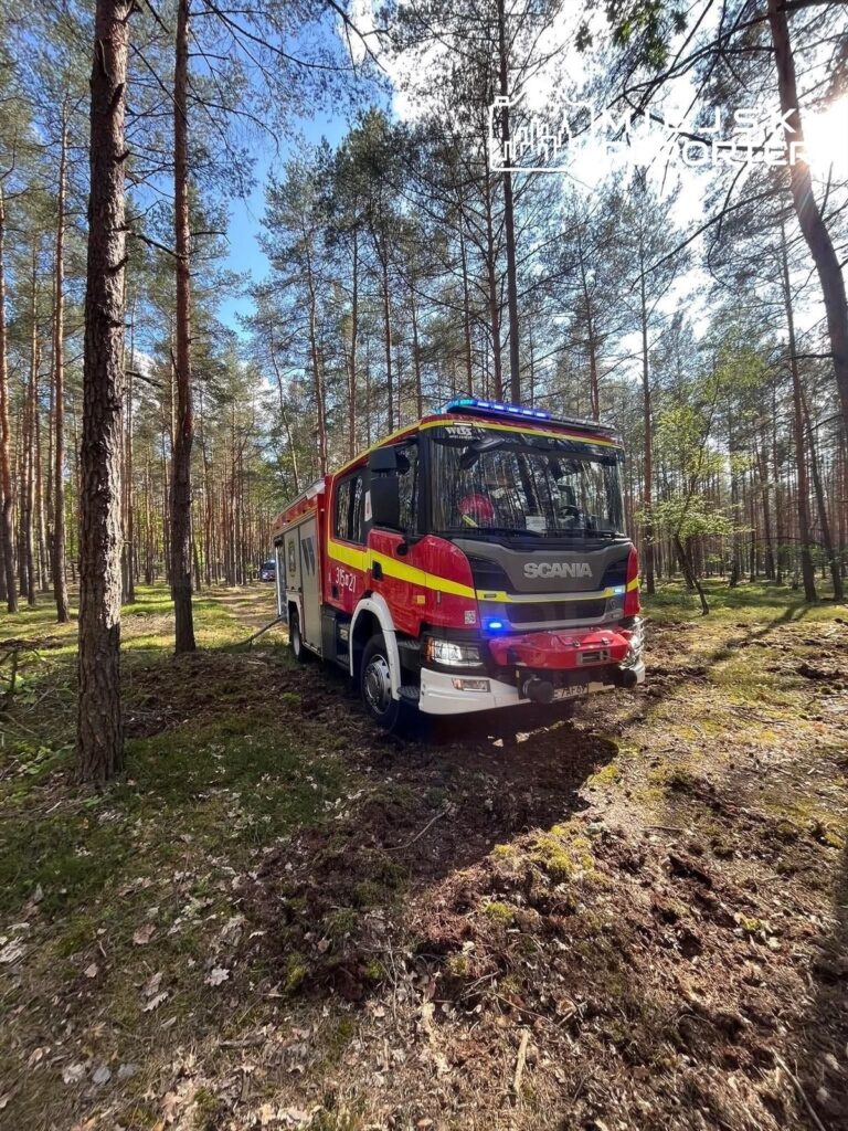 Wóz strażacki marki Scania zatrzymany w lesie, otoczony przez wysokie drzewa i zieleń.