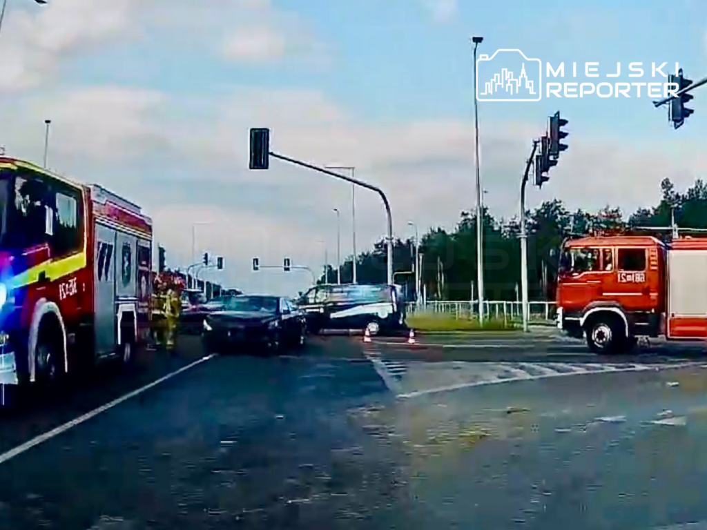 Na skrzyżowaniu zatrzymane pojazdy, w tym woz strażacki, a obok strażacy zabezpieczają miejsce zdarzenia.