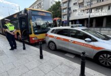 Mężczyzna w mundurze stoi obok przystanku, obok zatrzymanego autobusu i samochodu służby nadzoru ruchu.