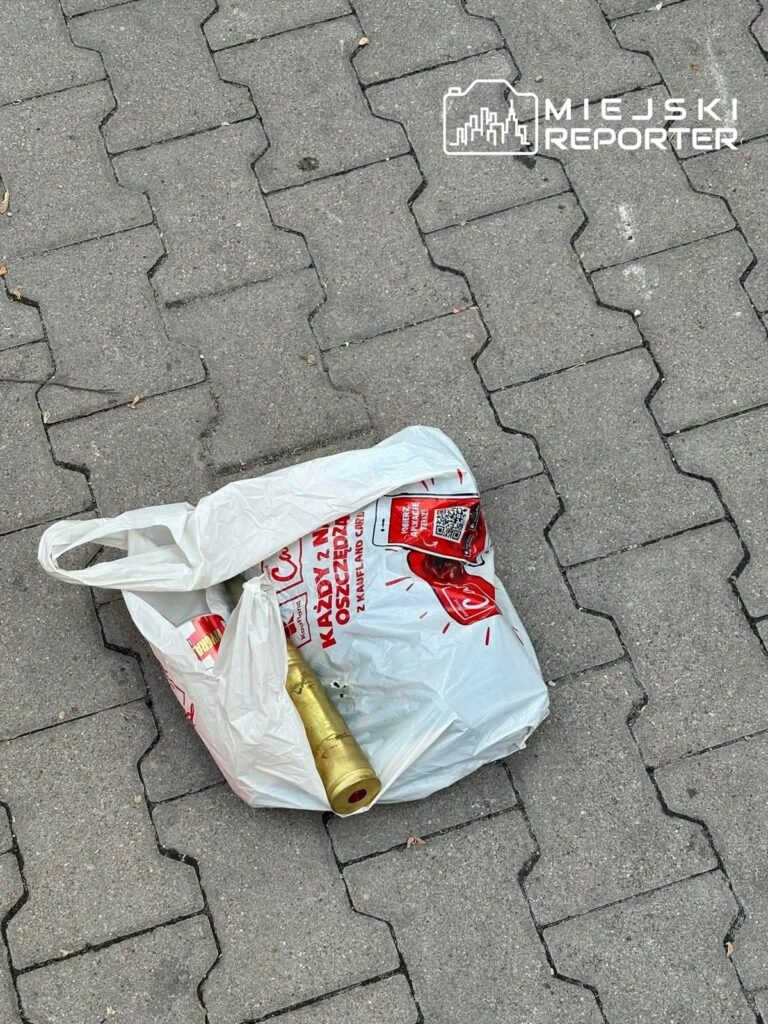Złota butelka leży w białej torbie na chodniku z szarych płytek.