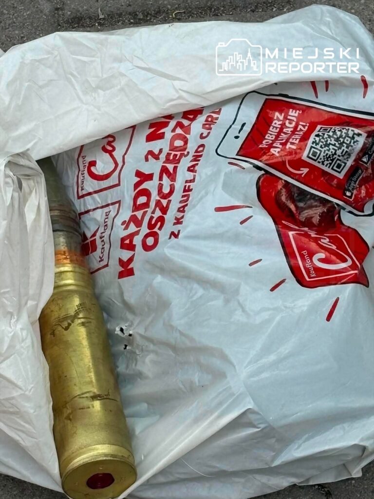 Metalowy przedmiot przypominający pocisk leży obok reklamowej torby z logo supermarketu.