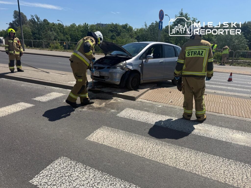 Strażacy zabezpieczają miejsce wypadku drogowego, gdzie samochód osobowy stoi na pasach.