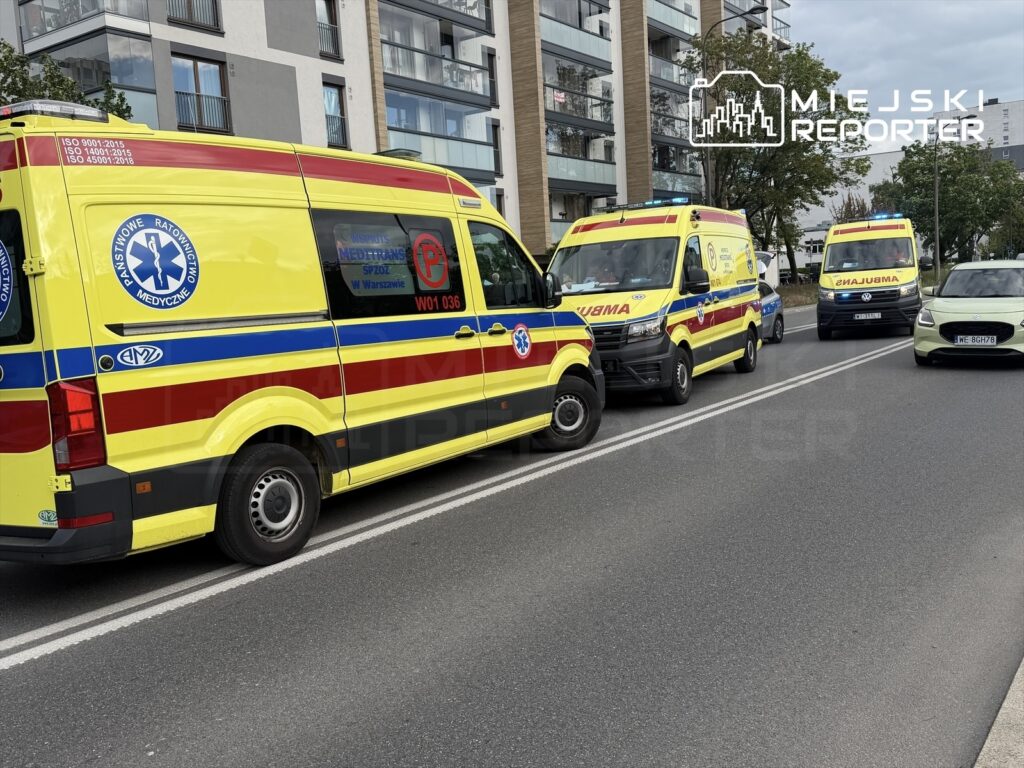 Zespół trzech ambulansów w żółto-czerwonych barwach zaparkowanych na ulicy obok nowoczesnych budynków mieszkalnych.