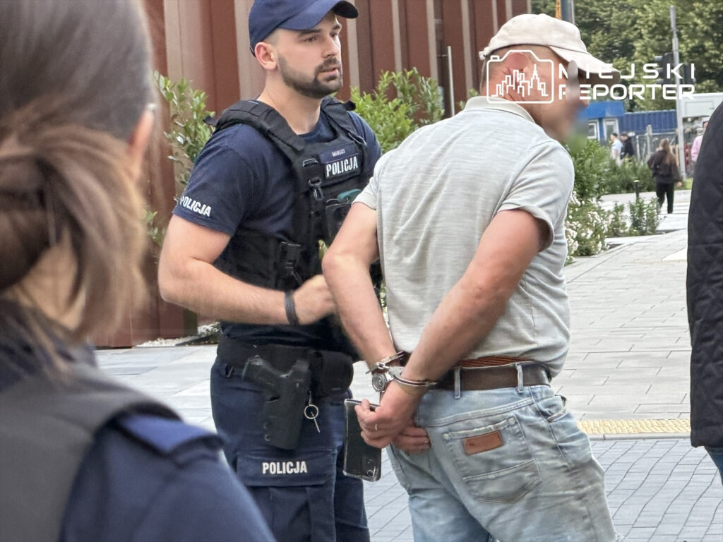 Policjant w mundurze zatrzymuje mężczyznę w kajdankach na miejskiej ulicy.