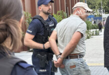 Policjant w mundurze zatrzymuje mężczyznę w kajdankach na miejskiej ulicy.