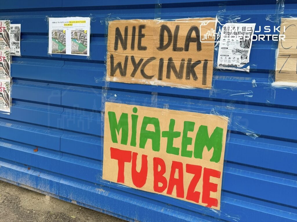 Na niebieskiej ścianie widoczne są dwa kartony z hasłami: "NIE DLA WYCIŃKI" oraz "MIAŁEM TU BAZĘ". Obok znajdują się plakaty.