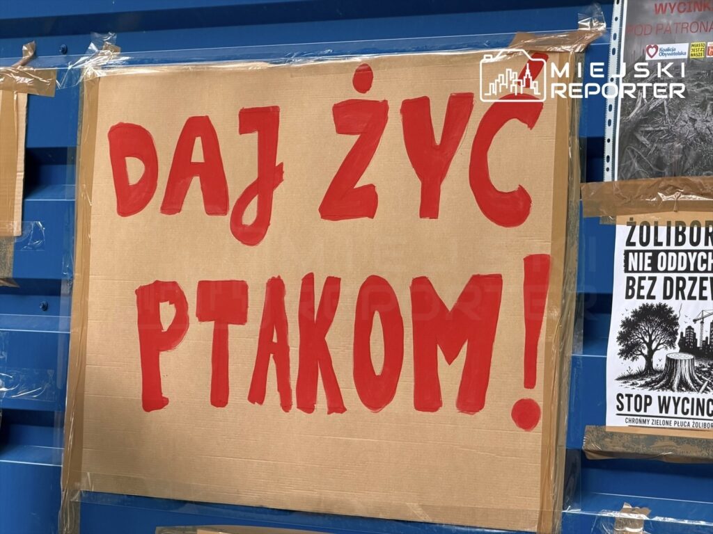 Na tekturowym plakacie widnieje napis „DAJ ŻYĆ PTAKOM!” w dużych, czerwonych literach, umieszczony na niebieskim tle.