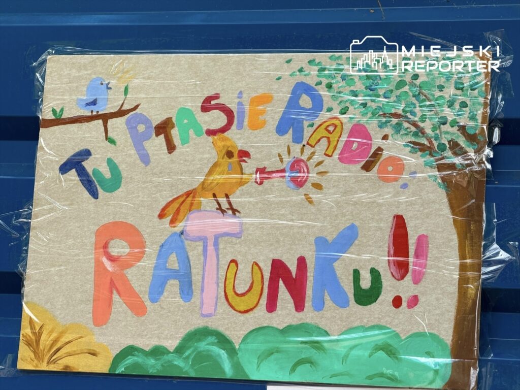 Kolorowy plakat z napisem "Tu Ptasie Radio. RATUNKU!!" i rysunkiem ptaka na tle zieleni.