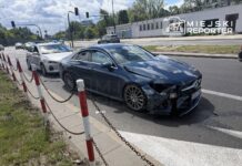 Nieoznakowany radiowóz policji stoi obok uszkodzonego samochodu osobowego z wgniecioną przednią częścią na drodze.