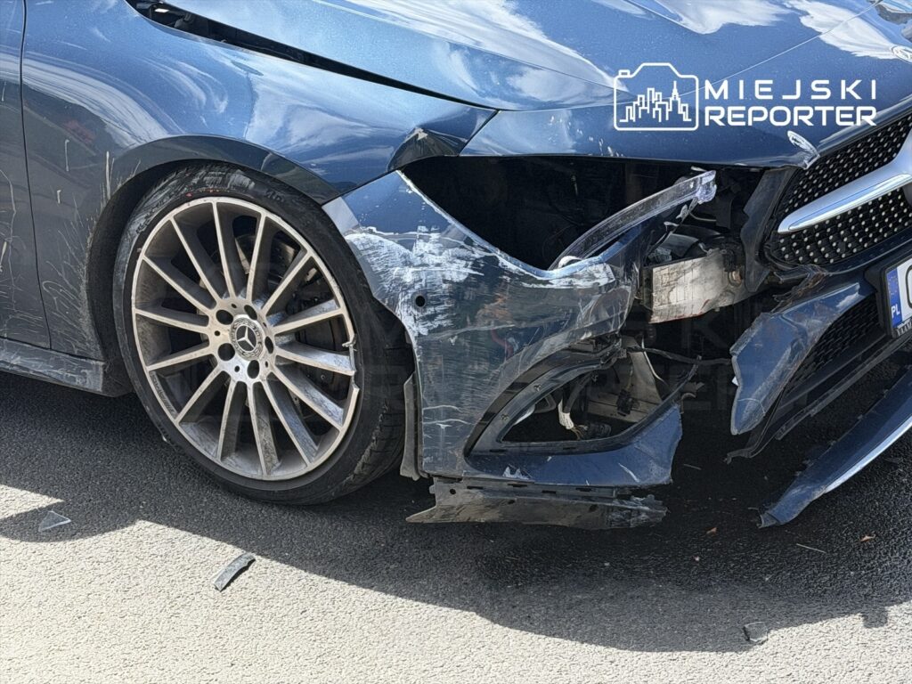 Uszkodzony niebieski samochód osobowy z poważnymi wgnieceniami w przednim zderzaku i zarysowaniami na nadwoziu.