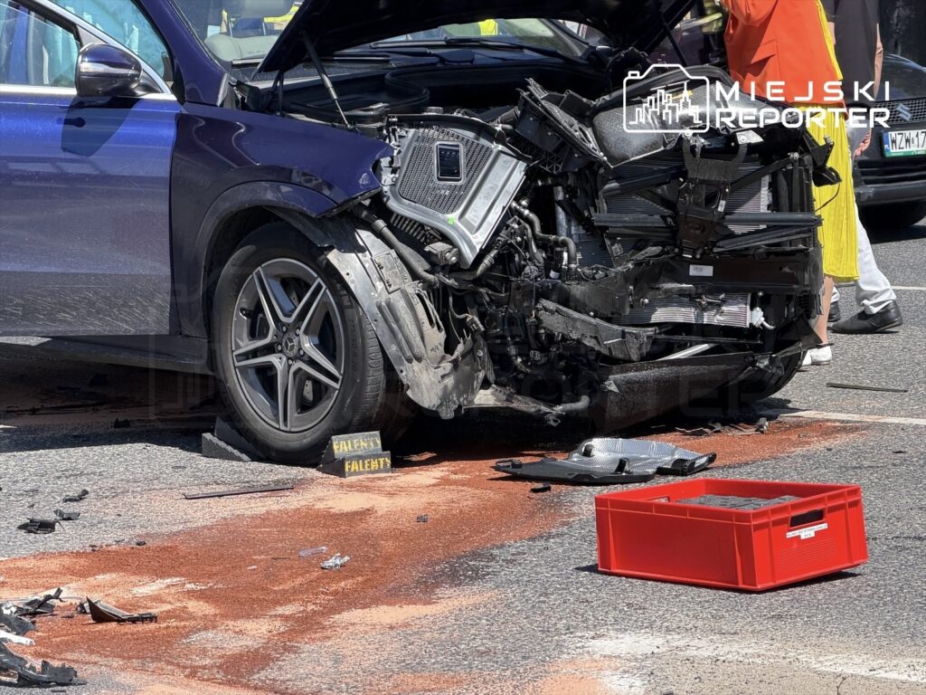 Uszkodzony samochód osobowy z rozbitą przednią częścią stoi na drodze, obok widać plamę cieczy i czerwony pojemnik.