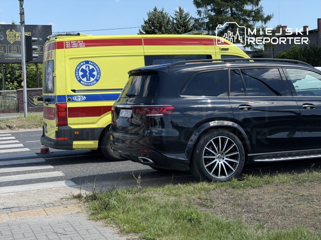 Karetka pogotowia ratunkowego zatrzymana obok czarnego SUV-a na drodze w słoneczny dzień.