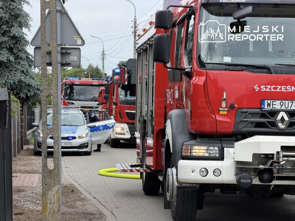 Czerwony wóz strażacki i policyjny samochód na ulicy, z otwartymi drzwiami i włączonymi sygnałami świetlnymi.