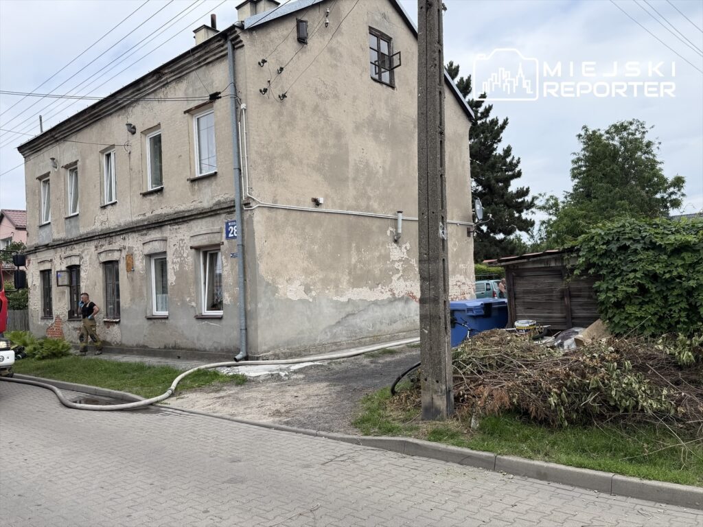 Mężczyzna w mundurze strażackim przebywa obok budynku mieszkalnego z widocznymi uszkodzeniami elewacji.