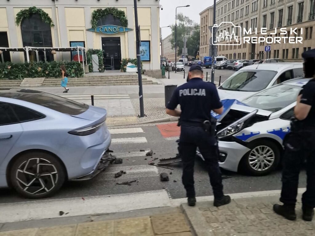 Policjanci badają kolizję dwóch samochodów na ulicy, obok restauracji z dużymi oknami.