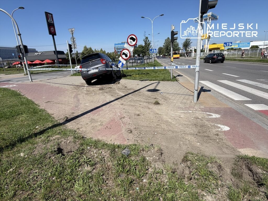 Czarny samochód osobowy wjeżdżający na chodnik obok znaku drogowym, w otoczeniu terenów handlowych.