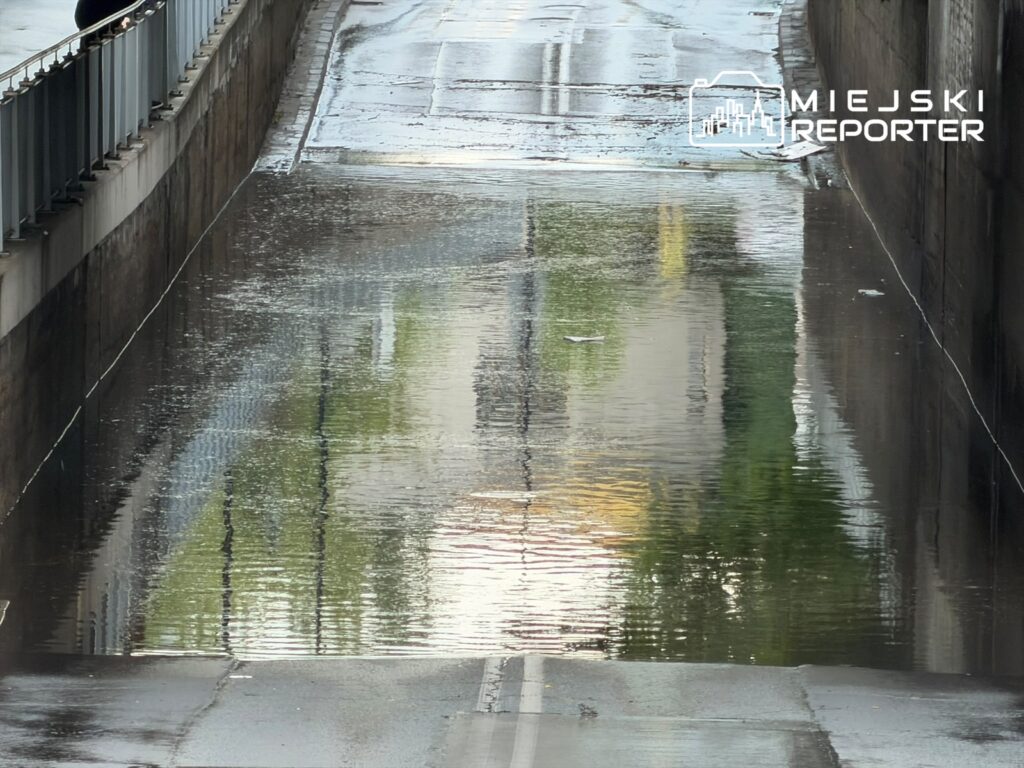Zalany tunel z odbiciem otaczających budynków na powierzchni wody.