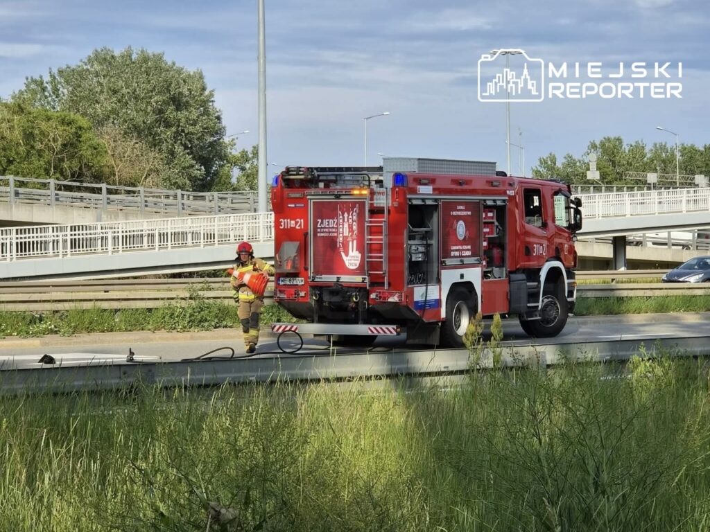Strażak w stroju ochronnym ustawia znaki ostrzegawcze obok wozu strażackiego na ruchliwej drodze.