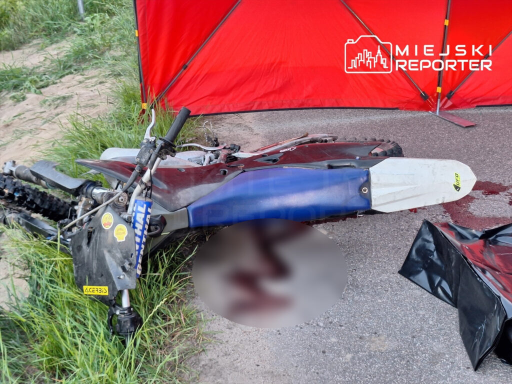 Zniszczony motorcrossowy motocykl leży na drodze, obok widoczne ślady krwi i czerwona płachta.