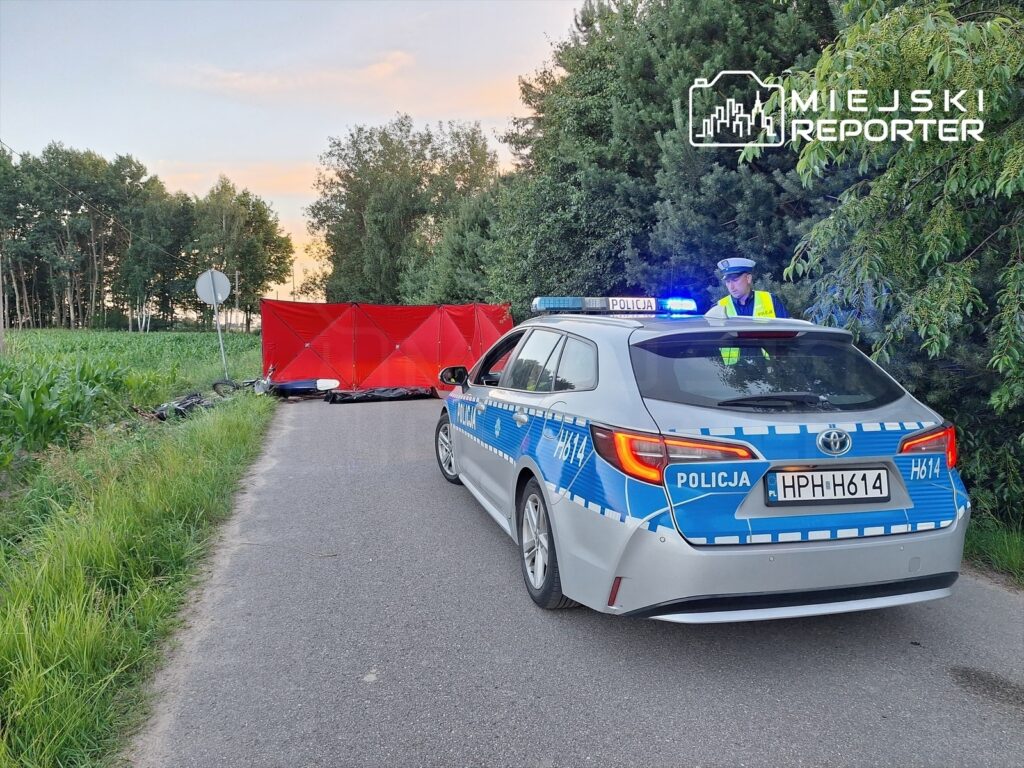 Policjant w kamizelce odblaskowej kontrolujący miejsce wypadku przy czerwonym namiocie wzdłuż drogi.