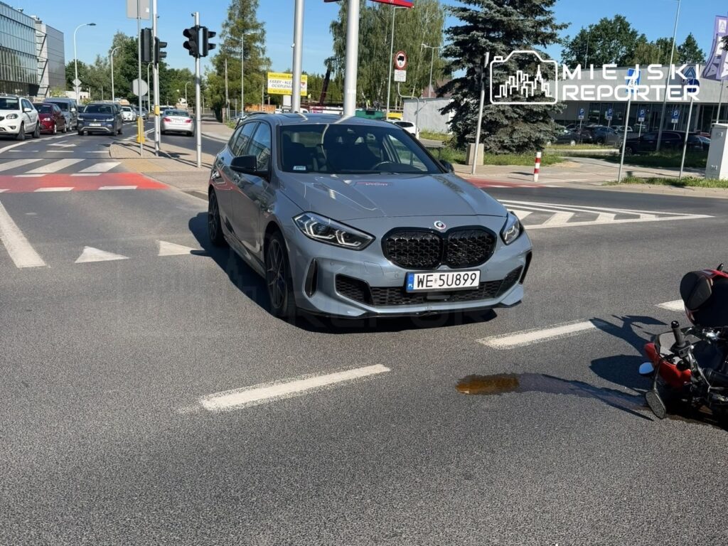 Szary samochód osobowy z dużym grillem stoi na skrzyżowaniu, obok leży rozlany płyn.