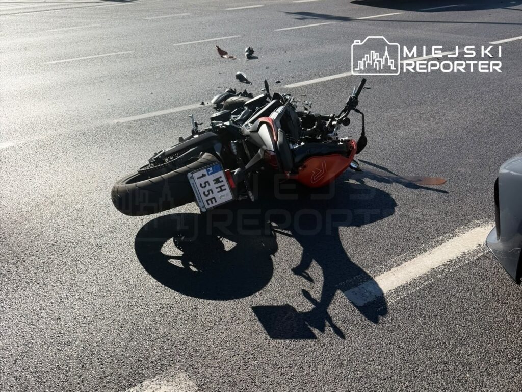 Motocykl leżący na boku na drodze, z uszkodzeniami i fragmentami pojazdu rozrzuconymi wokół.