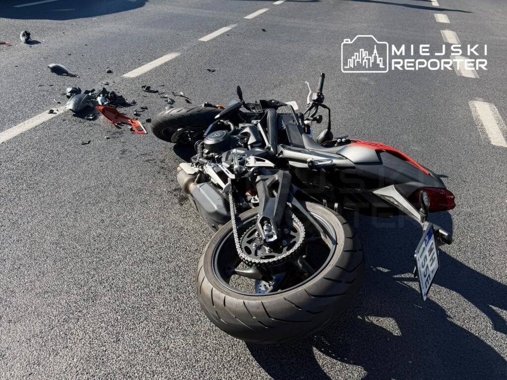 Motorower leży na jezdni, otoczony odłamkami części, po wypadku drogowym.