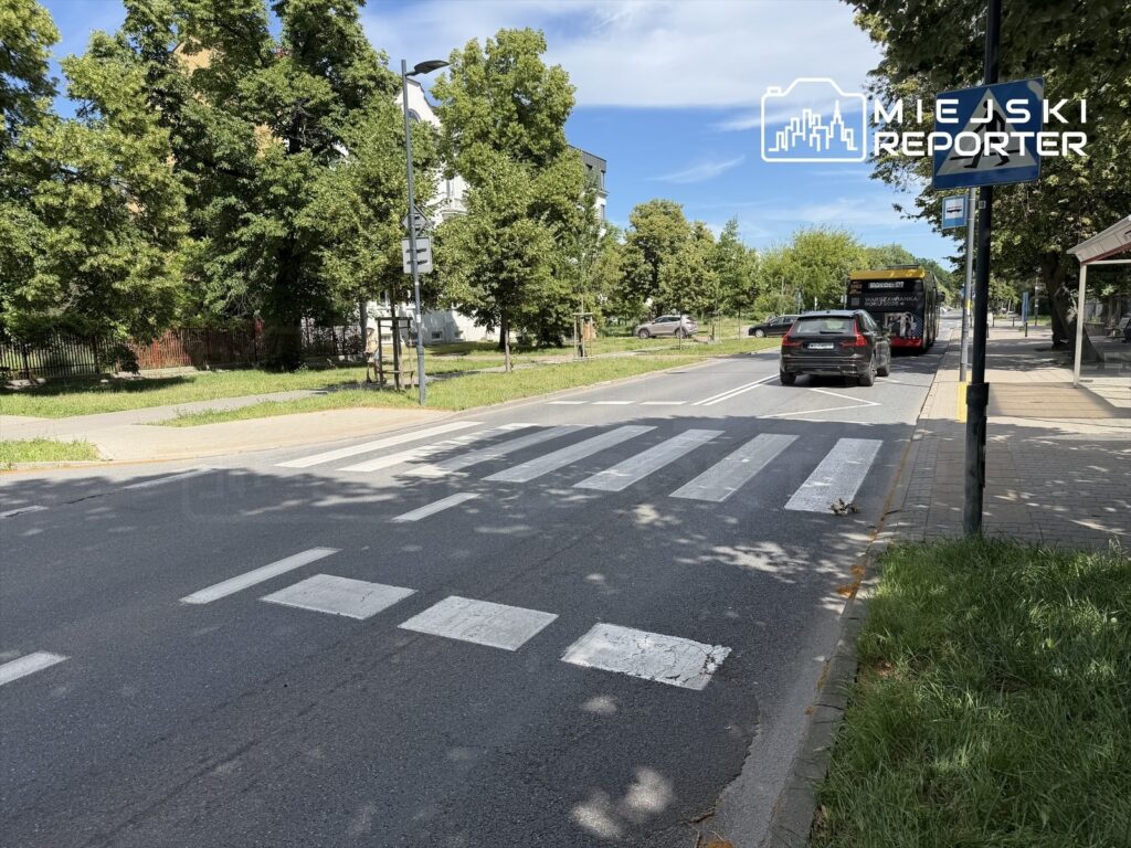 Kierowca w czarnym samochodzie zatrzymuje się przed przejściem dla pieszych na ulicy, obok przystanku autobusowego.
