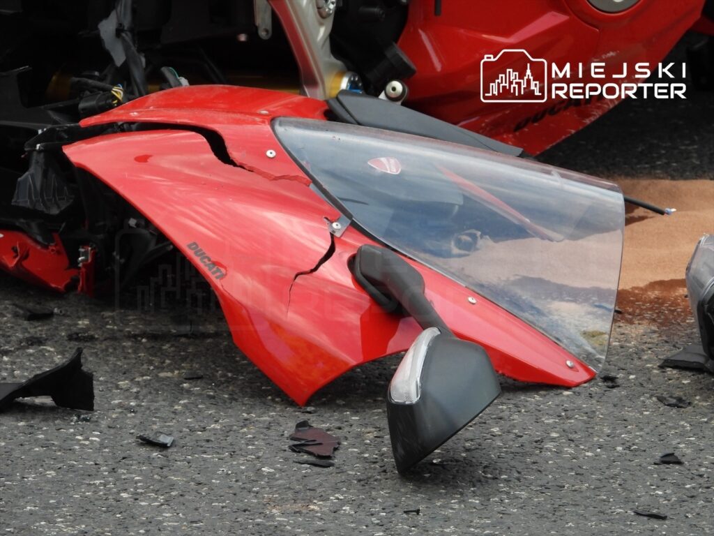 Złamana owiewka czerwonego motocykla marki Ducati leży na asfalcie obok resztek pojazdu.