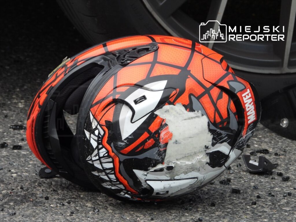 Uszkodzony kask motocyklowy z motywem Spider-Mana leży na asfalcie obok rozbitego szkła.