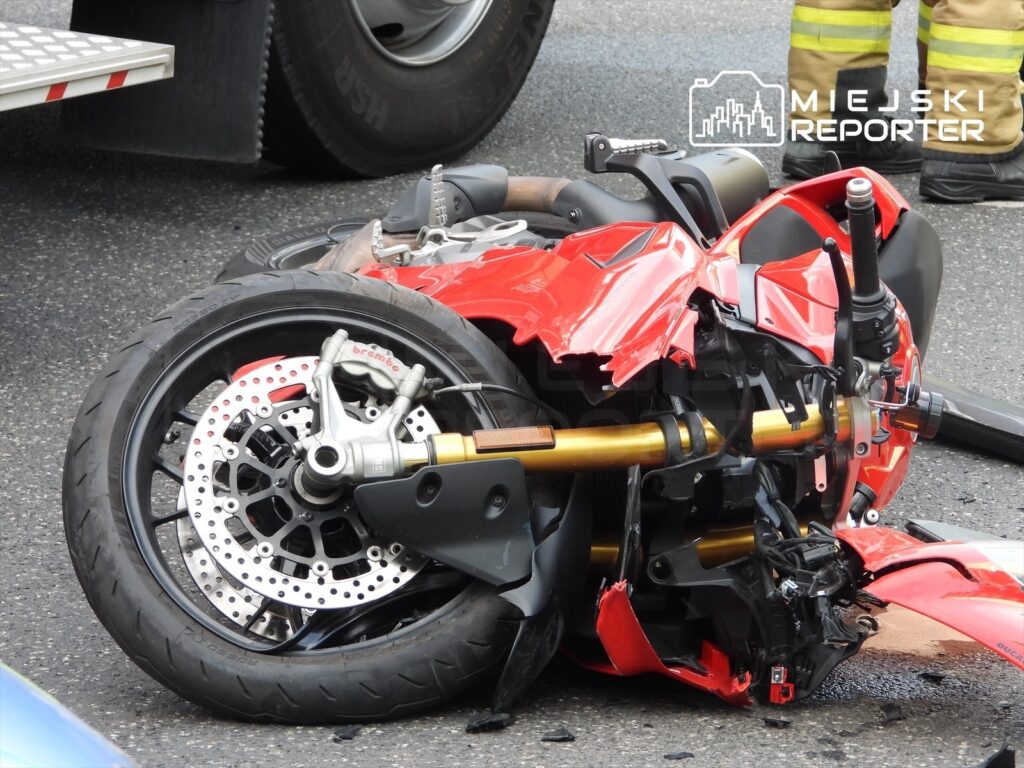 Zniszczony motocykl leży na drodze, obok widoczne są fragmenty uszkodzeń oraz koła.