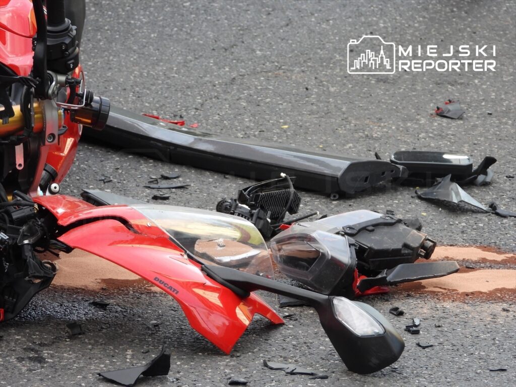 Zniszczony motocykl leży na asfalcie, wokół niego rozrzucone fragmenty karoserii i olej.