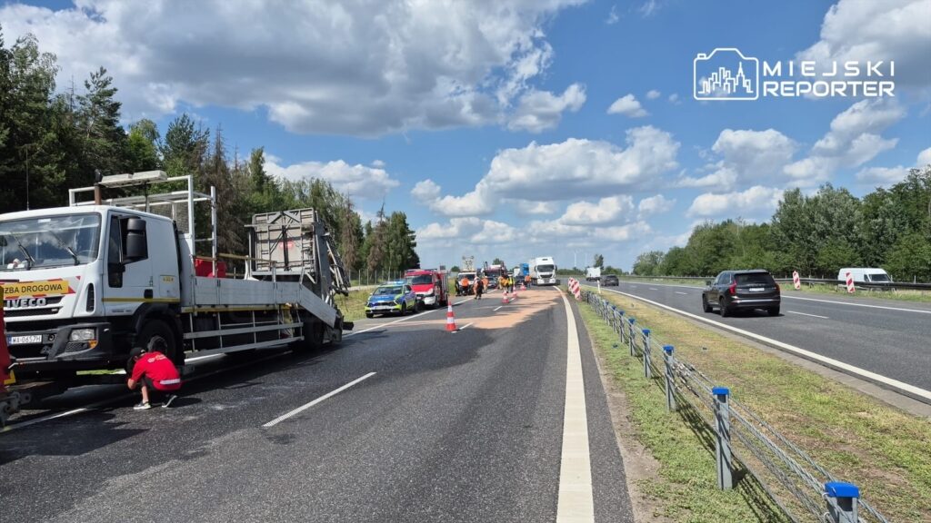 Na drodze krajowej trwa akcja naprawcza, z ciężarówką drogową oraz pracownikami w odblaskowych kamizelkach.
