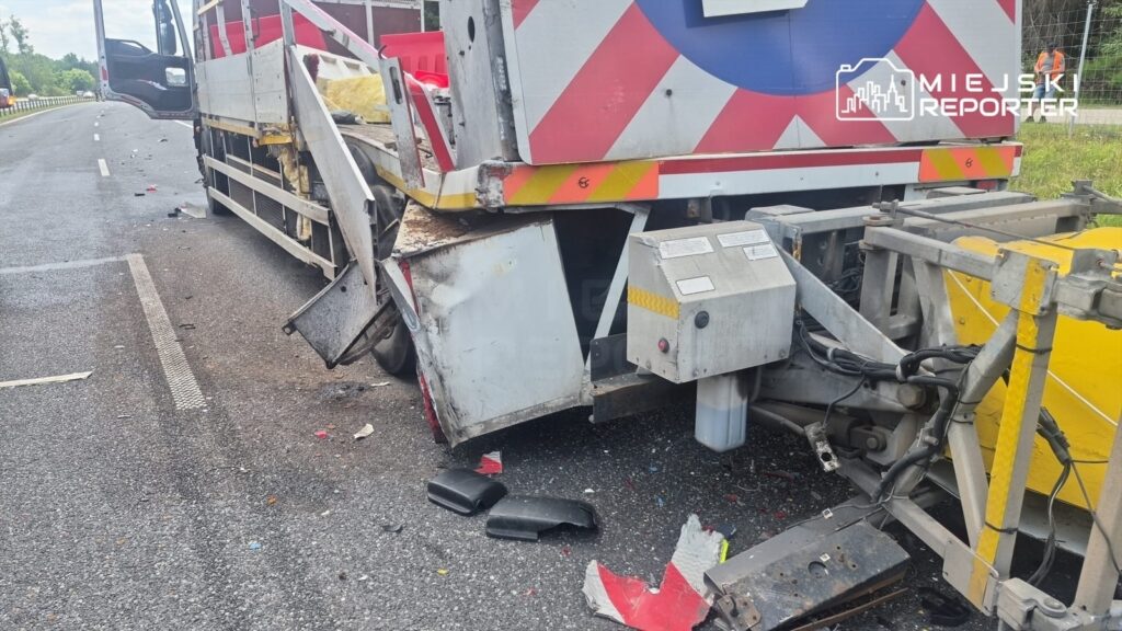 Uszkodzony pojazd ciężarowy z widocznymi śladami kolizji na poboczu drogi, w otoczeniu resztek materiałów.