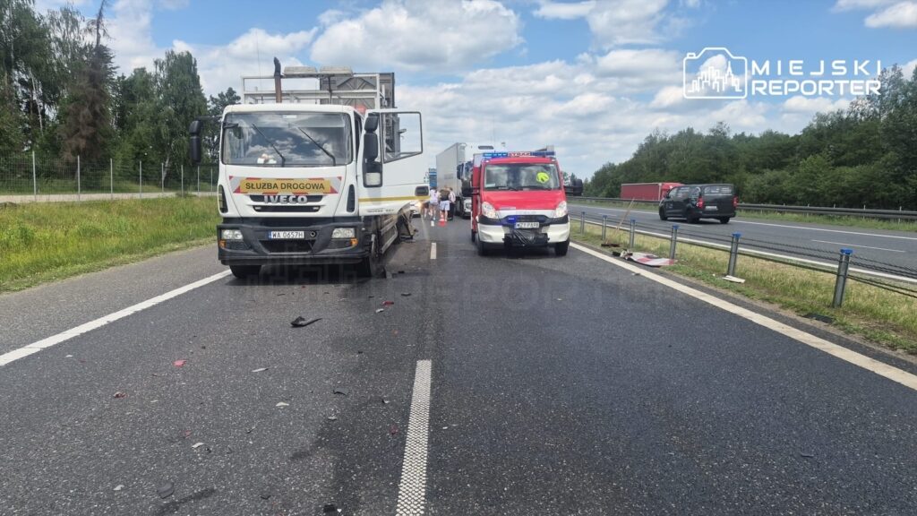 Na drodze stoi ciężarówka z napisem "Służba Drogowa", obok niej widać ambulans oraz grupę osób.