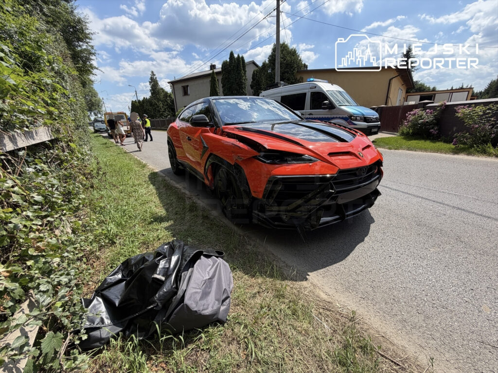 Czerwony samochód sportowy zaparkowany przy drodze, obok grupy osób rozmawiających z policjantem.