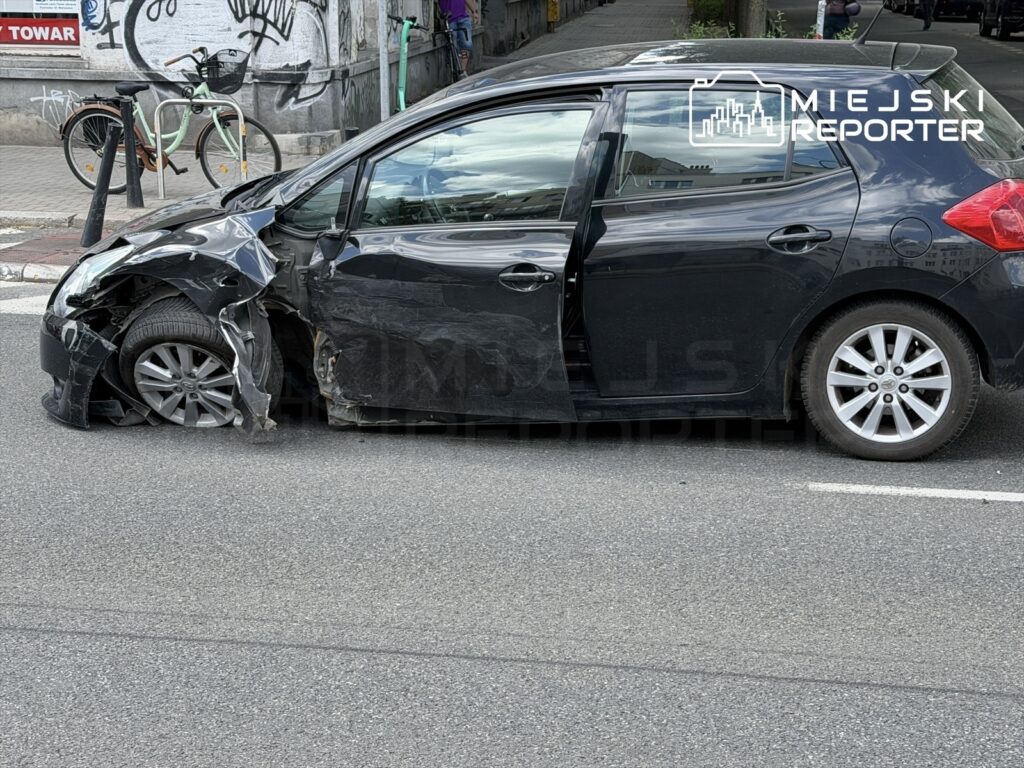 Czarny samochód osobowy z uszkodzoną karoserią zaparkowany na ulicy, z widoczną oponą w stanie deficytu.