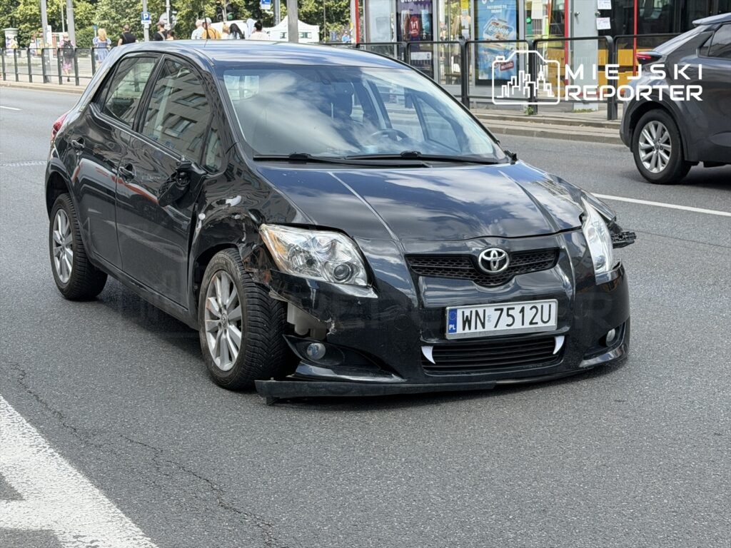 Czarny samochód osobowy z uszkodzoną przednią częścią stoi na ulicy w miejskim otoczeniu.