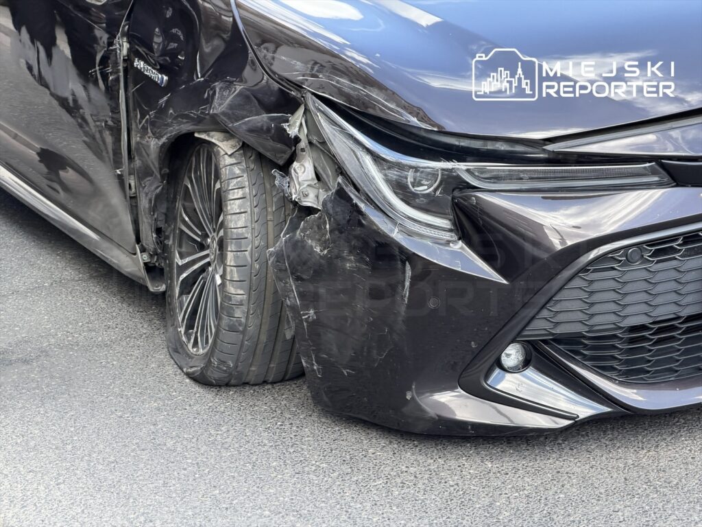 Czarny samochód osobowy z uszkodzeniami bocznymi, stojący na ulicy z widoczną zniszczoną felgą.