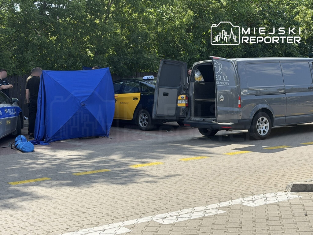 Grupa policjantów prowadzi działania w otoczeniu nieoznakowanego taxi i samochodu transportu pogrzebowego, osłoniętych niebieskim namiotem.