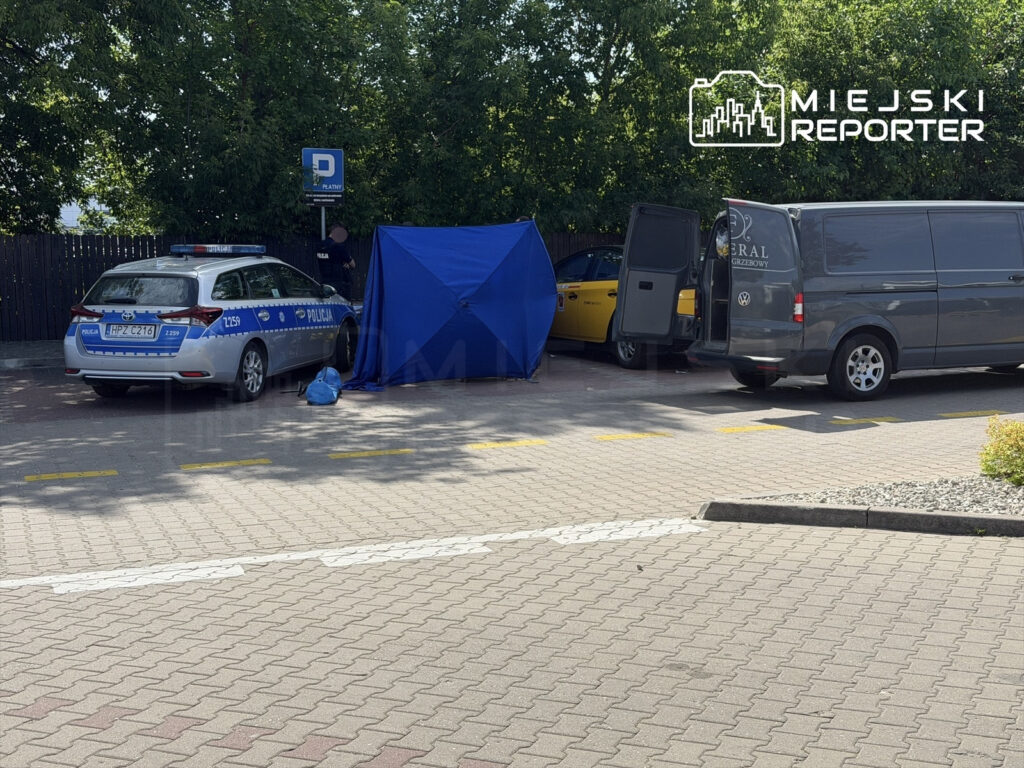 Policjant przy nieoznakowanym pojeździe policyjnym zabezpiecza miejsce zdarzenia, obok rozstawiony niebieski namiot.