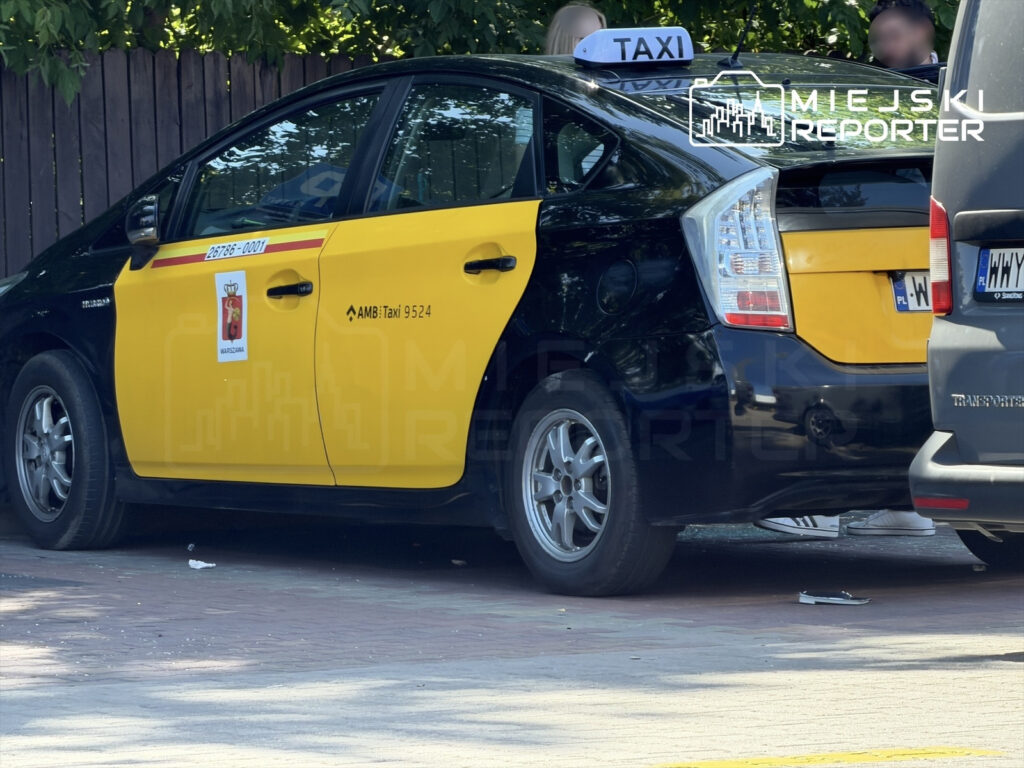 Taxi z żółtym i czarnym malowaniem zaparkowane na ulicy, z widocznym napisem "TAXI" na dachu.