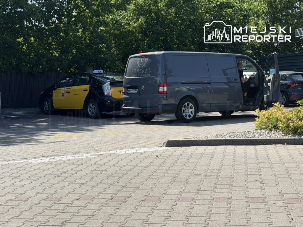 Szary samochód dostawczy z otwartymi drzwiami zaparkowany przy czarnym taksówce na parkingu.